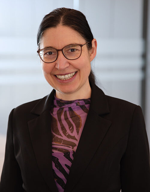 Mit einem freundlichen Lächeln präsentiert sich die Frau in einem professionellen Outfit, ideal für ein Unternehmensumfeld.