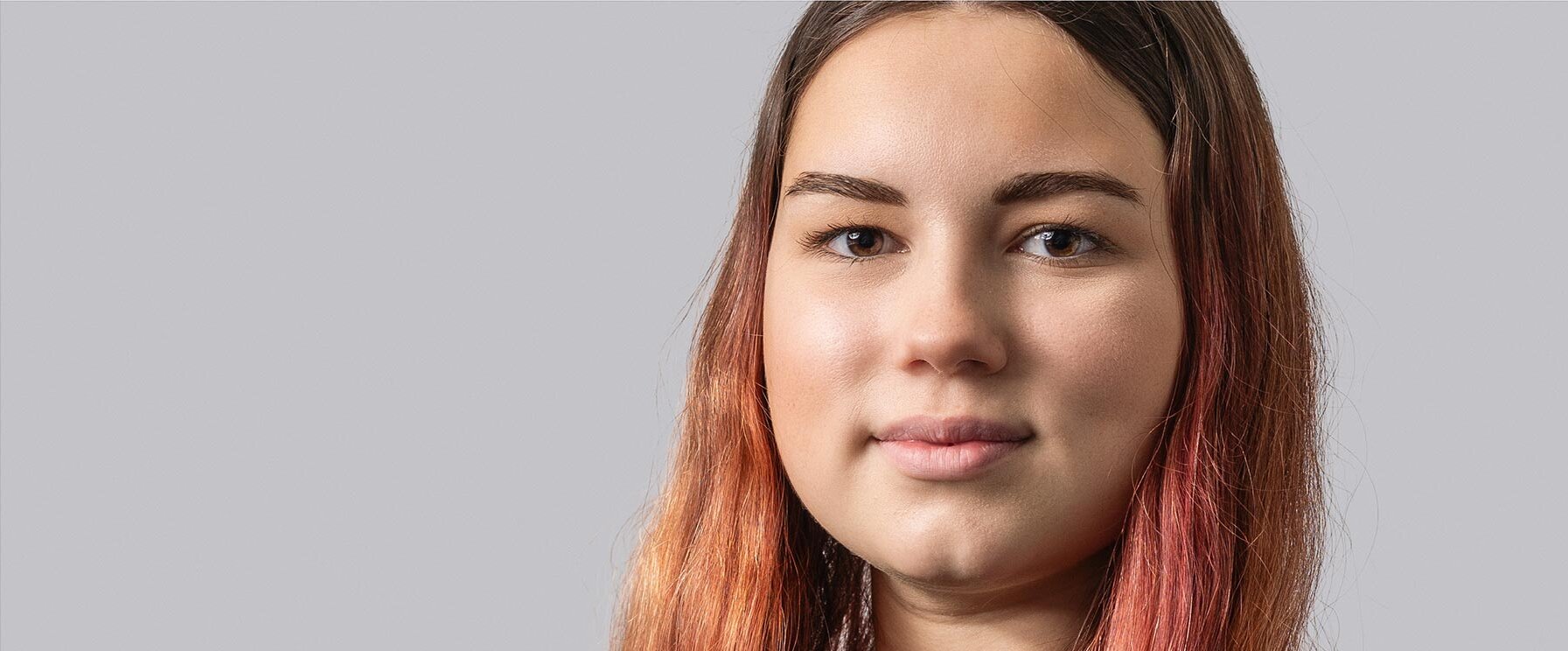 Eine junge Frau mit langen, rot gefärbten Haaren blickt direkt in die Kamera und strahlt Selbstbewusstsein aus.