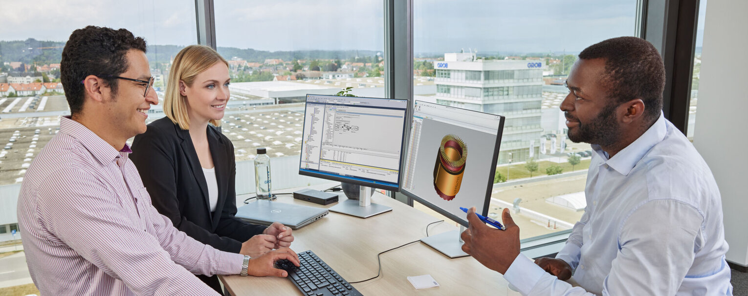 Drei Fachleute bei GROB diskutieren an einem Tisch über technische Zeichnungen und 3D-Modelle auf ihren Bildschirmen.