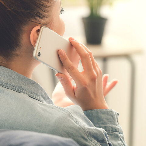 Eine Person spricht am Telefon, während sie entspannt in einem modernen Raum sitzt, mit einer Pflanze im Hintergrund.
