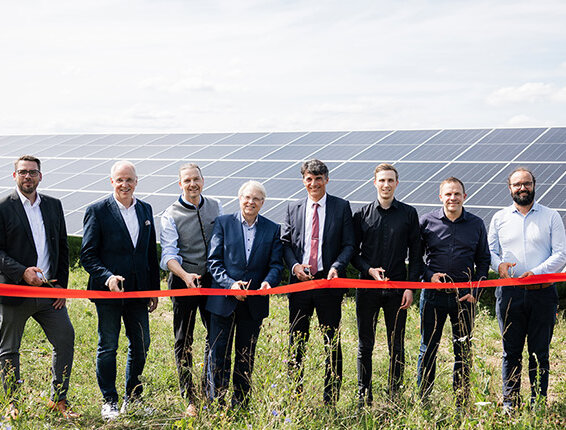 Die Eröffnungszeremonie zeigt mehrere Männer, die ein rotes Band vor einer Solaranlage durchtrennen, um Nachhaltigkeit zu feiern.