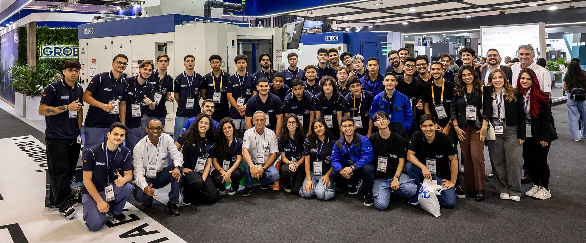 Ein fröhliches Team von GROB steht vor einer hochmodernen Maschine, die auf der Expomafe 2025 in São Paulo ausgestellt ist.