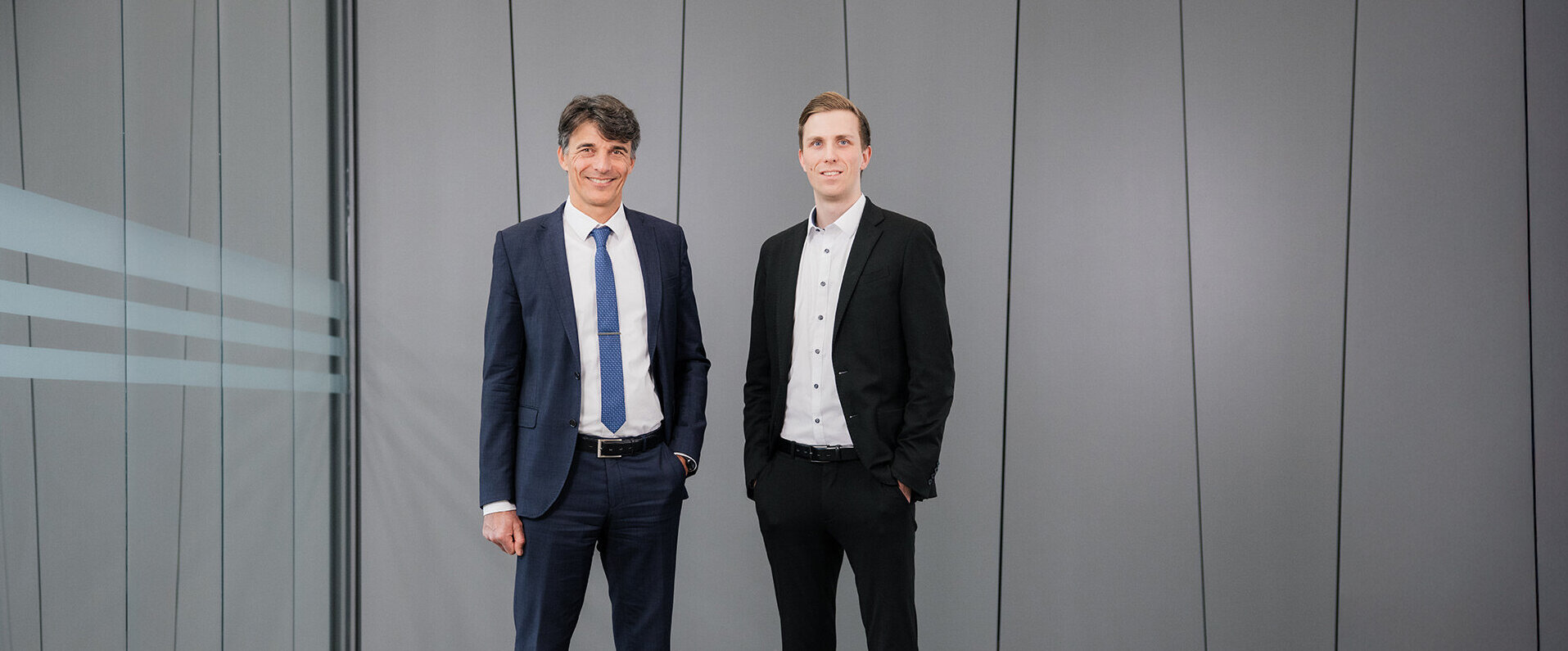 Christian Grob und Florian Grob stehen in einem modernen Büro mit grauen Wänden und einem eleganten Bodenbelag.