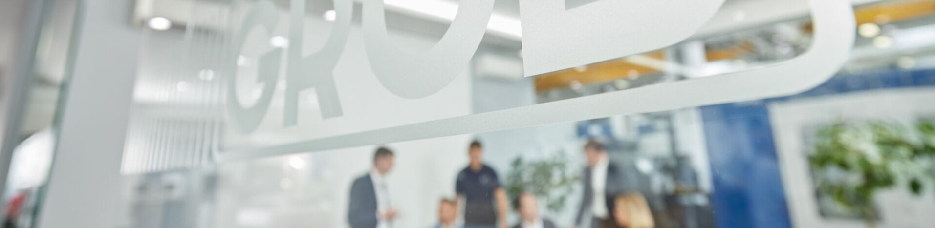 Das GROB-Logo ist klar erkennbar, während Mitarbeiter in einem eleganten Büro an einem Projekt arbeiten.