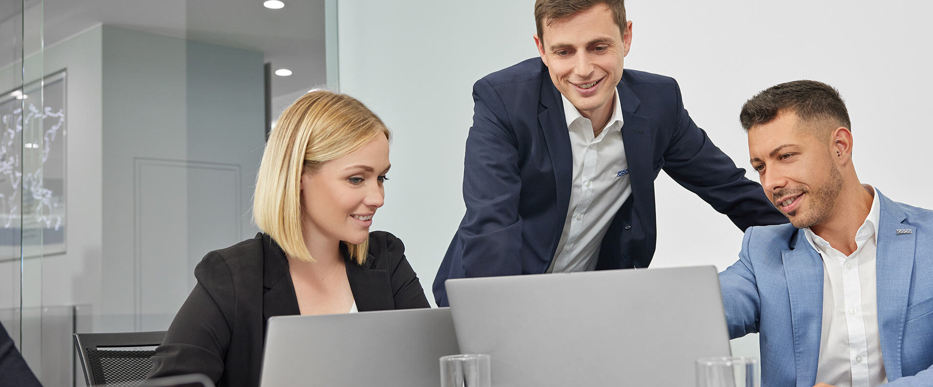Drei Fachleute in einem modernen Konferenzraum arbeiten gemeinsam an Laptops und diskutieren angeregt über ein Projekt.