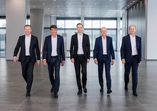 Die Geschäftsleitung von GROB schreiten in eleganter Kleidung durch einen lichtdurchfluteten Raum, der Professionalität ausstrahlt.