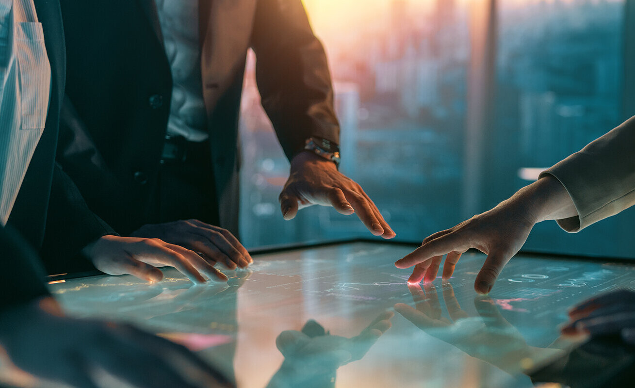 Mehrere Personen in Anzügen interagieren mit einem digitalen Touchscreen, während sie strategische Ideen diskutieren.