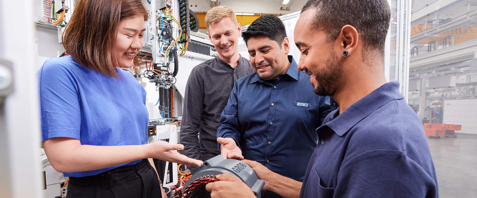 Eine Gruppe von vier Personen in einem modernen Arbeitsumfeld diskutiert begeistert über ein technisches Bauteil.