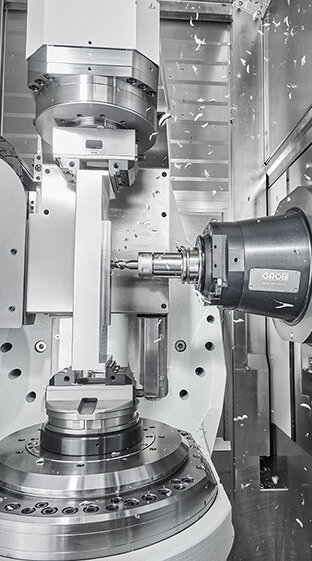Eine hochmoderne GROB-Maschine bearbeitet präzise Metallteile, während Späne durch die Luft fliegen.