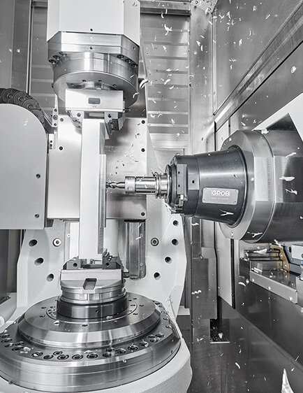 Eine hochmoderne GROB-Maschine bearbeitet präzise Metallteile, während Späne durch die Luft fliegen.