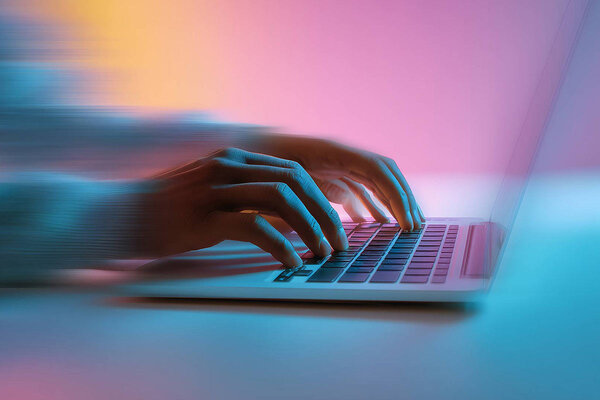 Eine Hand tippt schnell auf einer Laptop-Tastatur, umgeben von einem sanften, farbigen Lichtspiel.