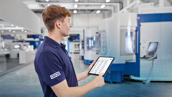 Ein Mitarbeiter von GROB steht in einer modernen Fertigungshalle und nutzt ein Tablet zur Überwachung von Maschinen.