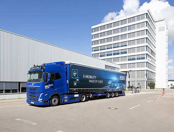 Der E-Lkw mit dem Logo von GROB zeigt die Zukunft der E-Mobilität, während er vor einem eleganten, modernen Gebäude parkt.