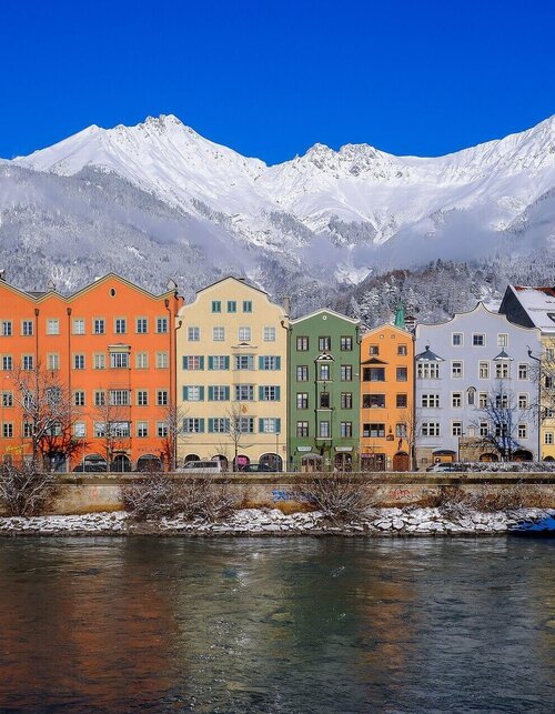 Bunte Häuser am Fluss mit schneebedeckten Bergen im Hintergrund Bunte Häuser am Fluss mit schneebedeckten Bergen im Hintergrund