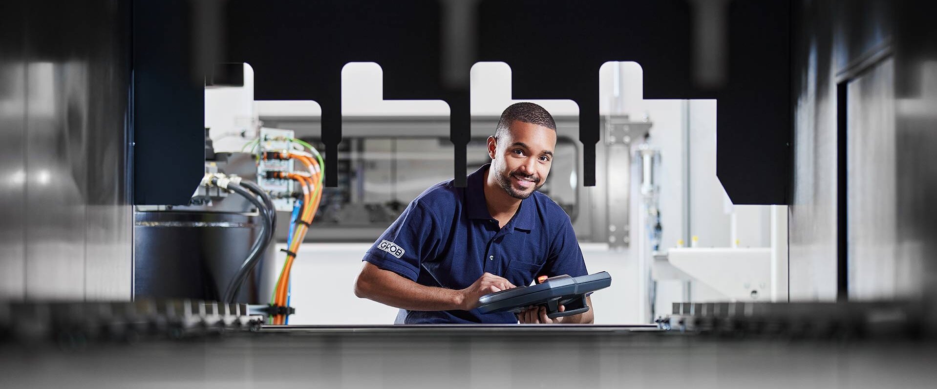 In einer hochmodernen Produktionsstätte von GROB arbeitet ein Techniker mit einem Bedienfeld und zeigt dabei Freude.