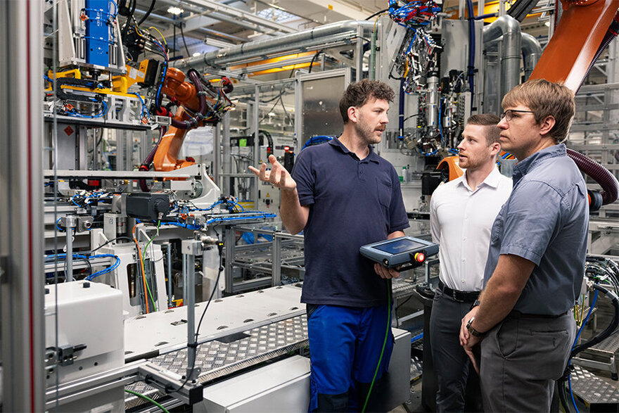 Ein Team von GROB bespricht innovative Technologien in einer automatisierten Produktionslinie mit einem Roboter im Hintergrund.