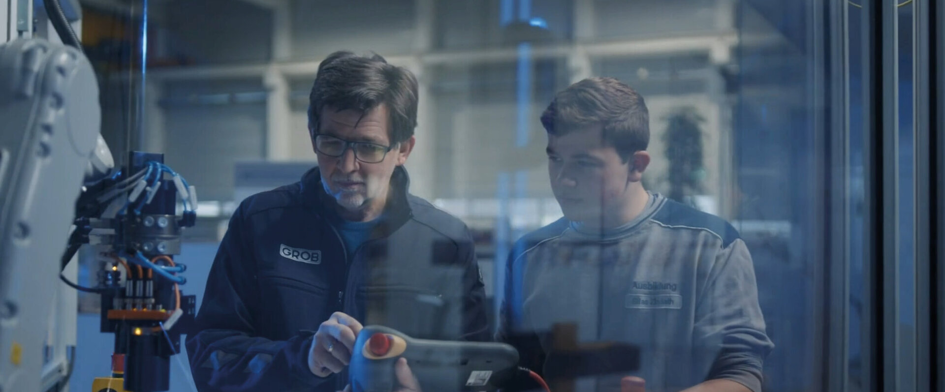 Ein erfahrener Techniker und ein Auszubildender betrachten gemeinsam ein Steuergerät in einer modernen Werkstatt.