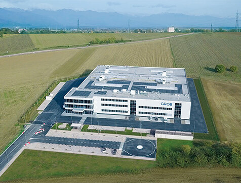 Das GROB-Werk in Italien ist von einer gepflegten Landschaft umgeben, mit einem klaren Himmel und sanften Hügeln im Hintergrund.
