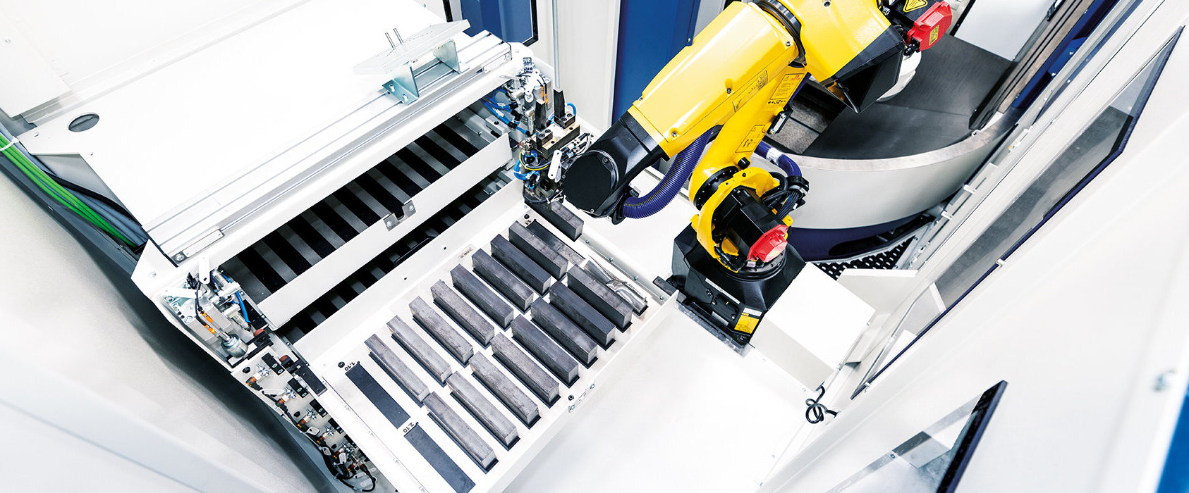 Ein gelber Industrieroboter greift präzise Metallteile aus einer automatisierten Fertigungszelle von GROB.