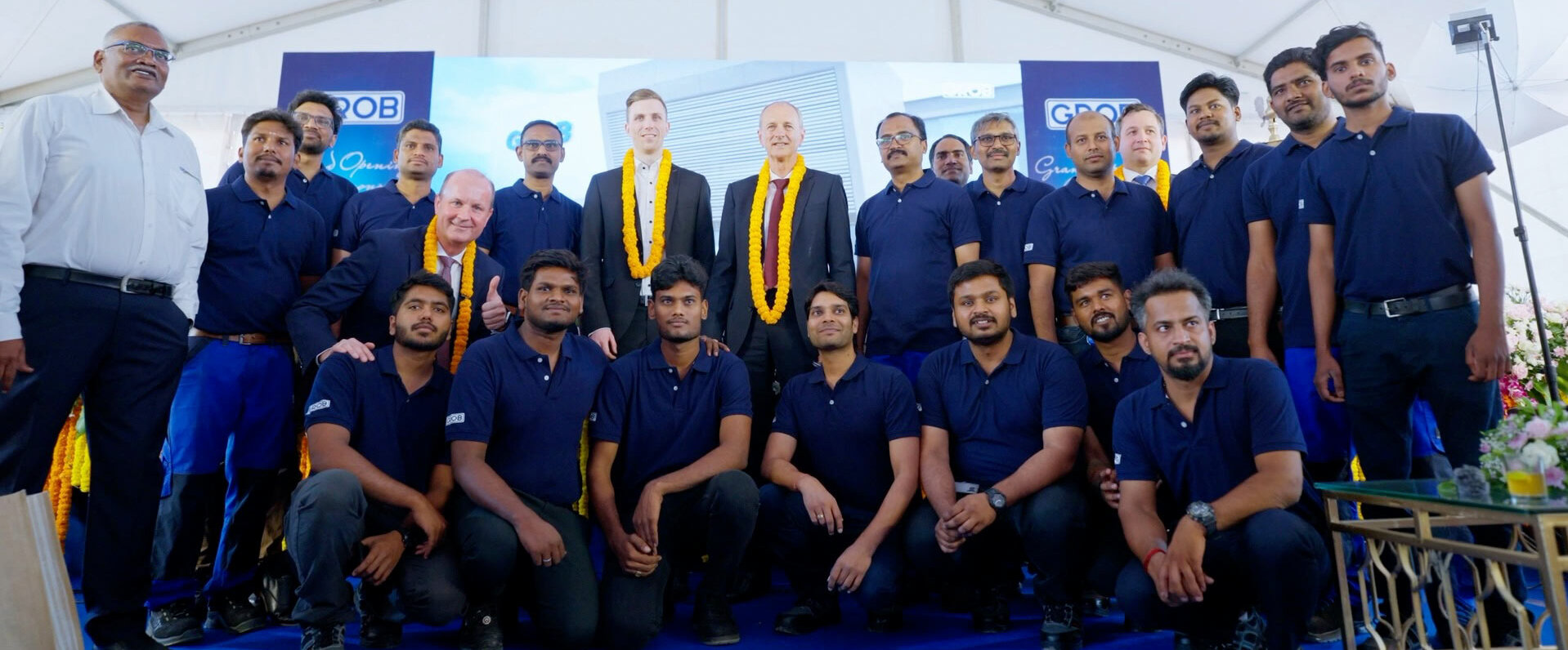 Ein Team von GROB-Mitarbeitern steht zusammen, um den neuen Standort in Bangalore zu feiern, mit einer festlichen Dekoration im Hintergrund.